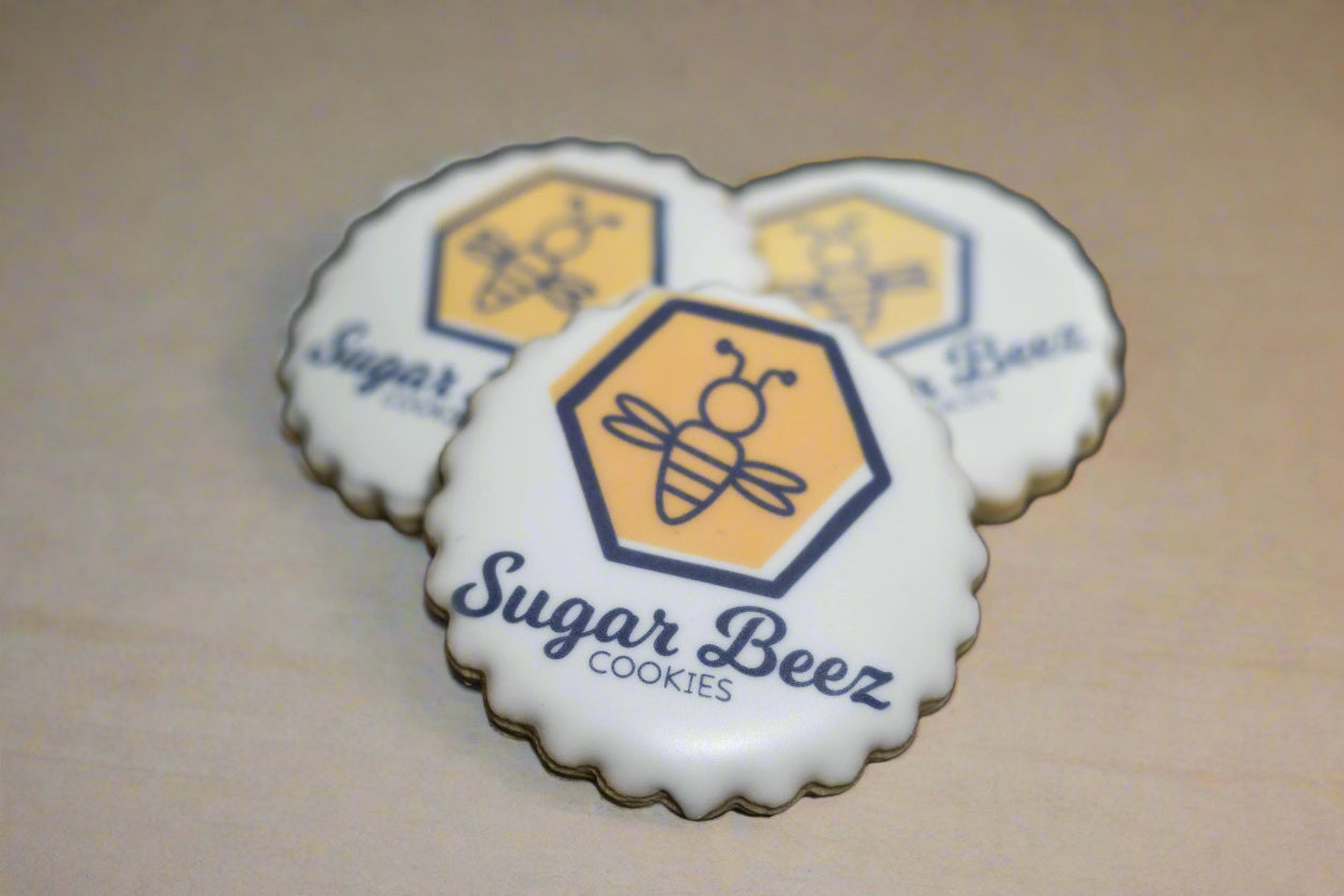 Round scalloped cookie with Sugar Beez logo printed on white icing.