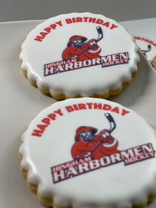 Round scalloped cookie with Happy Birthday and Hingham Harbormen Hockey logo printed on white icing.