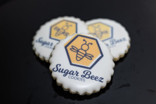 Round scalloped cookie with Sugar Beez logo printed on white icing.